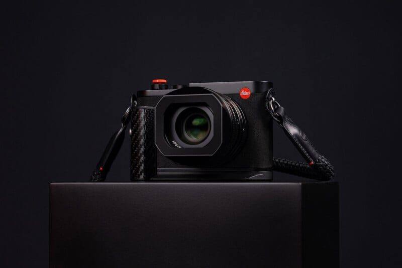 The Leica Q3 43 Formula 1 Edition on its display stand, showing the carbon fibre handgrip and the red-rimmed soft release button.