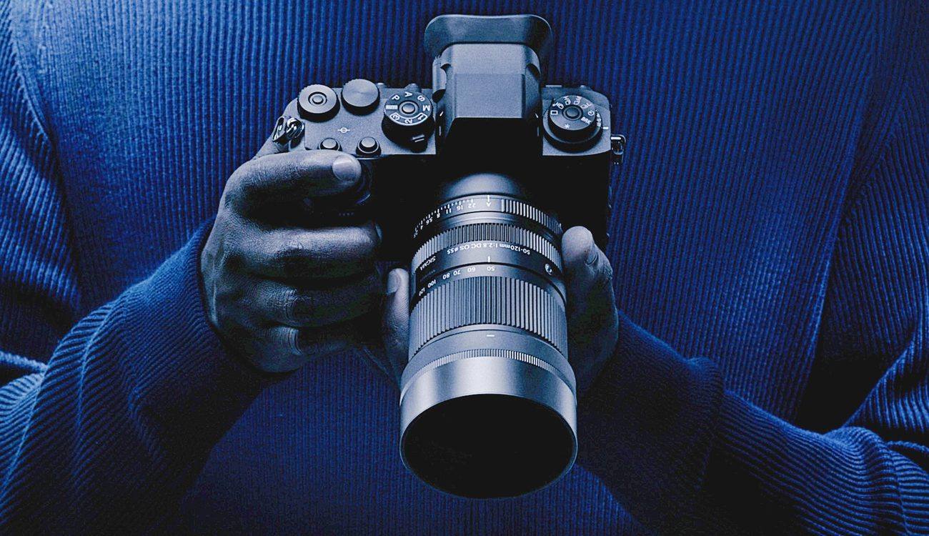The Sigma 50-120mm F2.8 DC OS Contemporary mounted on a Fujifilm X mount camera and held in both hands, in Sigma's campaign photograph for the lens announced on October 8, 2026.
