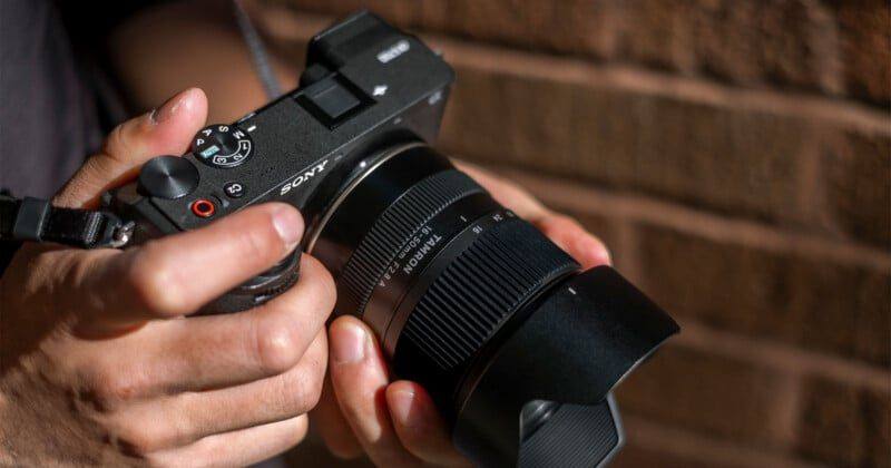 The Tamron 16-50mm F2.8 A mounted on a Sony APS-C body and held in both hands, with its flower shaped hood fitted.