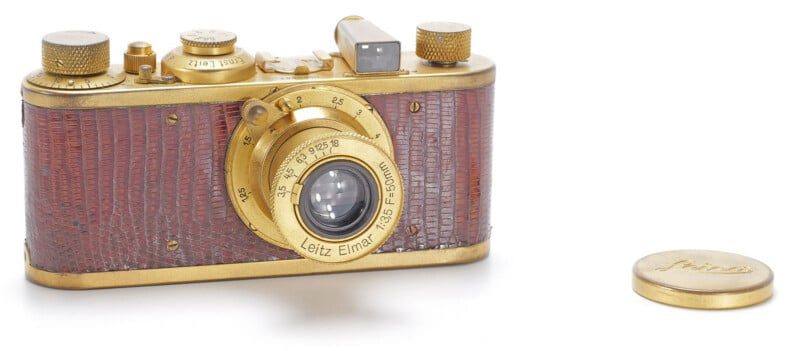 The gold-plated Leica I Model C Luxus of 1931, with brown leatherette and its lens cap beside it, which sold for 375,000 euros at Wetzlar.